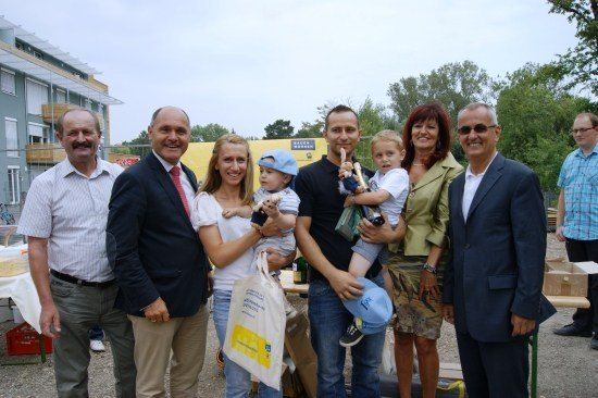 Eine Gruppe von Erwachsenen und Kindern posiert für ein Foto vor einem Gebäude mit gelber Wand und Bäumen im Hintergrund.