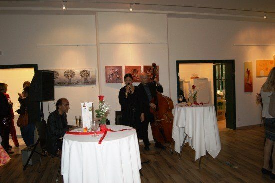 Ein Mann und eine Frau spielen auf der Bühne mit Cello und Mikrofon in einem Indoor-Veranstaltungsort. Ein Tisch mit Blumen und einer Schleife steht vor ihnen.