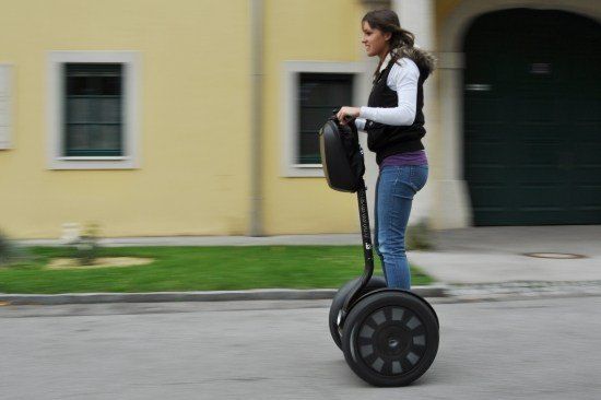 Eine Frau fährt einen Segway auf einer Straße mit einem gelben Gebäude im Hintergrund.