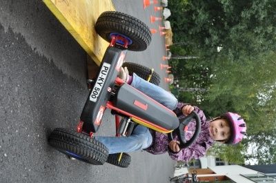 Ein kleines Kind mit einem rosa Helm fährt auf einer asphaltierten Straße mit einem roten Go-Kart mit der Nummer 500.