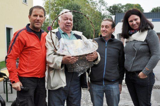 Vier Menschen stehen zusammen draußen, ein Mann hält einen mit Plastik bedeckten Korb.