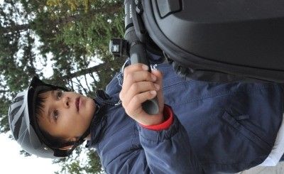 Ein junger Junge, der eine blaue Jacke und einen Helm trägt, hält mit der rechten Hand einen schwarzen Lenker und posiert möglicherweise für ein Foto.