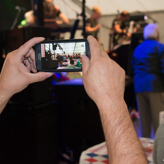 Eine Person macht ein Foto einer Live-Band-Aufführung mit einem Smartphone, das eine Menge zeigt, die die Musik genießt.