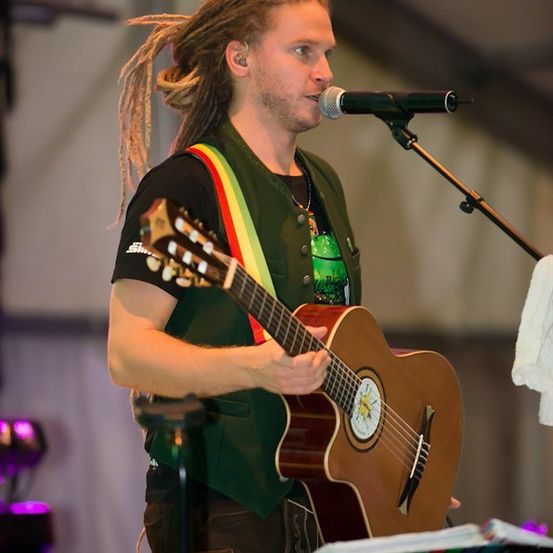 Ein Mann mit Dreadlocks steht auf der Bühne, spielt Gitarre und singt in ein Mikrofon.
