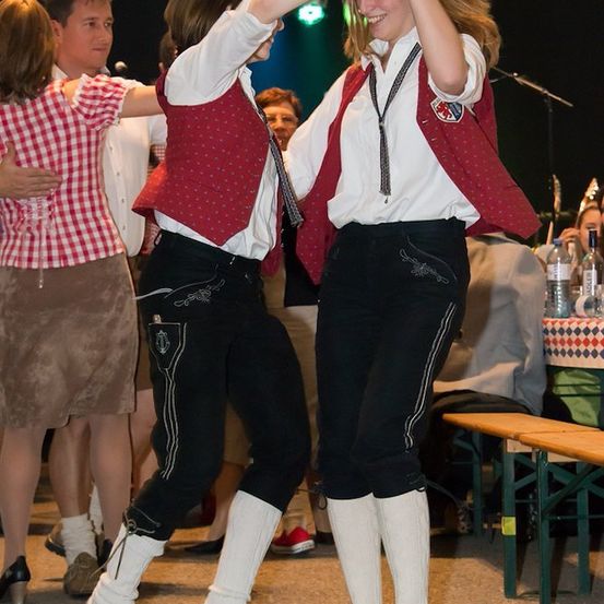 Zwei Frauen in traditioneller deutscher Kleidung tanzen bei einem Fest zusammen, lächeln und genießen es.