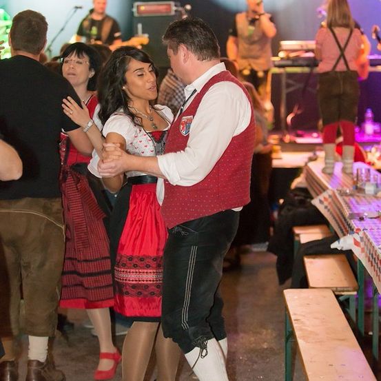 Ein Paar tanzt in traditioneller Kleidung bei einer lebhaften Veranstaltung, während eine Band im Hintergrund spielt.