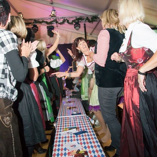 Eine Gruppe von Menschen in traditioneller Kleidung steht um einen langen Tisch mit Essen und Getränken, möglicherweise bei einem Festival.