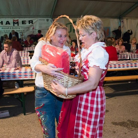 Zwei Frauen in traditioneller deutscher Kleidung halten einen Korb und lachen in einer festlichen Umgebung.