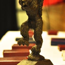 Eine Bronzestatue eines Bären, der auf seinen Hinterbeinen steht, auf einem Holzblock platziert, umgeben von roten Büchern auf einem Tisch.