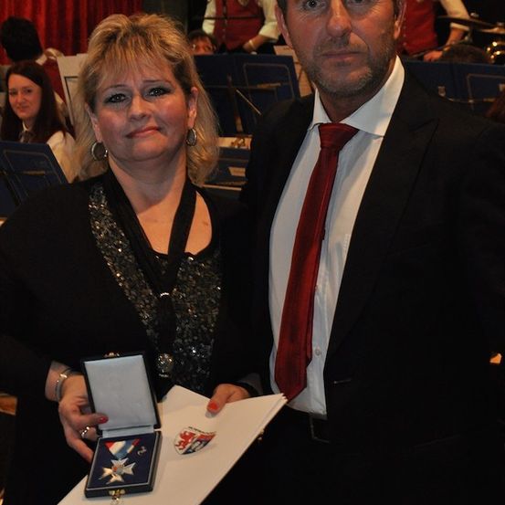 Ein Mann und eine Frau stehen zusammen und halten eine gerahmte Auszeichnung, mit einem verschwommenen Band im Hintergrund.