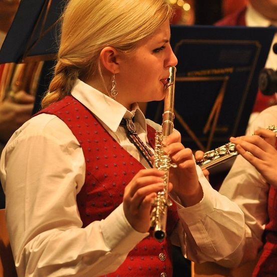 Eine Frau in einer roten Weste spielt während einer musikalischen Aufführung eine Flöte. Sie konzentriert sich auf ihr Instrument.