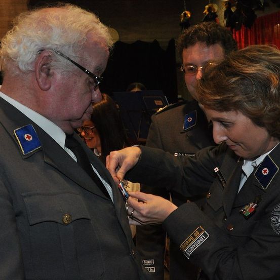 Eine Frau in Uniform steckt eine Medaille an die Revers eines älteren Mannes in Uniform.
