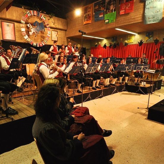 Ein Orchester spielt auf der Bühne mit einem Dirigenten vor ihnen. Das Publikum sitzt vor ihnen.