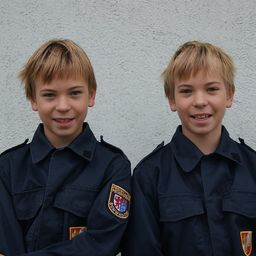 Zwei junge Jungen in dunkelblauen Uniformen mit Abzeichen auf der linken Brust lächeln und posieren für ein Foto.