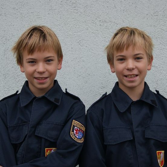Zwei junge Jungen in dunkelblauen Uniformen mit Abzeichen auf der linken Brust lächeln und posieren für ein Foto.