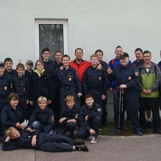 Eine Gruppe uniformierter Personen, einschließlich Erwachsener und Kinder, posiert für ein Foto vor einem Gebäude. Einige stehen, andere sitzen und eine Person liegt.