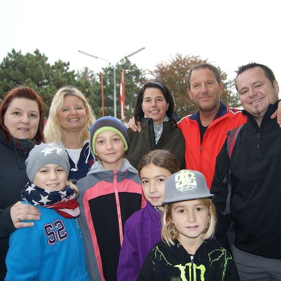 Eine Familie von sieben, einschließlich zwei Männern und fünf Kindern, lächelt für ein Gruppenfoto im Park.