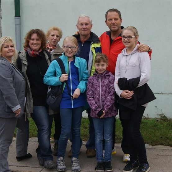 Eine Familie von sieben Personen, darunter zwei Erwachsene und fünf Kinder, steht gemeinsam auf einem Bürgersteig und lächelt für ein Foto.