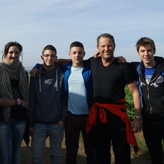 Fünf Menschen stehen lächelnd für ein Foto in einem Feld. Der Mann in der Mitte hat seine Arme um die Schultern zweier Jungen gelegt. Eine Frau links trägt eine Schürze.