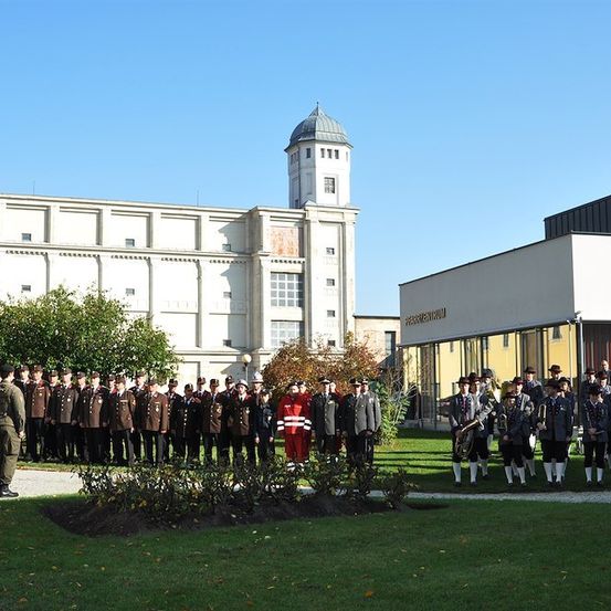 Eine Gruppe von Militärangehörigen in Uniform steht in Formation auf einem Rasen vor einem Gebäude mit einer Kuppelturm.