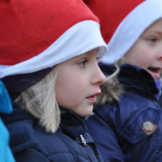 Zwei junge Mädchen mit roten und weißen Weihnachtsmützen, eines schaut nach vorne, das andere zur Seite.