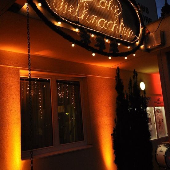 Ein Neonschild für 'Pinke Weihnachtsbaum' ist nachts beleuchtet und hängt über einem Gebäude mit einem Fenster und einem Drumset in der Nähe.
