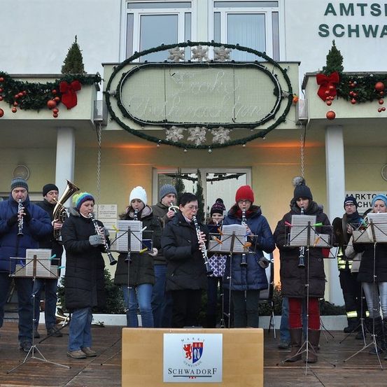 Eine Gruppe von Musikern in Winterkleidung spielt Instrumente auf einer Bühne vor einem geschmückten Gebäude.