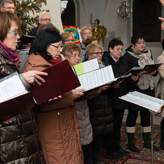 Eine Gruppe von Frauen in Winterkleidung steht und singt, während sie Bücher und Notenständer halten.