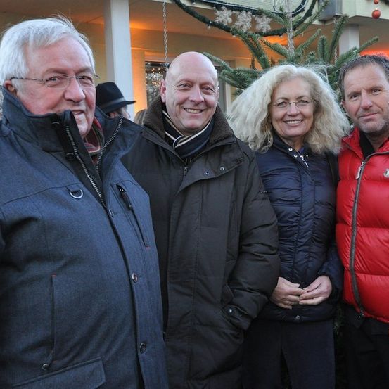 Vier Erwachsene, zwei Männer und zwei Frauen, stehen lächelnd vor einem geschmückten Weihnachtsbaum für ein Foto.