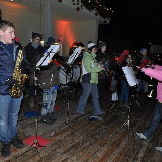 Eine Gruppe junger Musiker tritt bei Nacht auf einer Holzbühne auf, einer spielt Saxophon und andere verschiedene Instrumente.