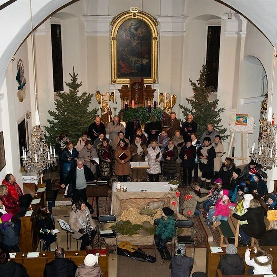 Eine Gruppe von Menschen versammelt sich in einer Kirche für einen Weihnachtsgottesdienst, mit Weihnachtsbäumen und einem geschmückten Altar im Hintergrund.