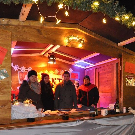 Vier Personen stehen in einer mit Weihnachtslichtern und Ornamenten geschmückten Holzhütte und lächeln für ein Foto bei einer festlichen Veranstaltung.