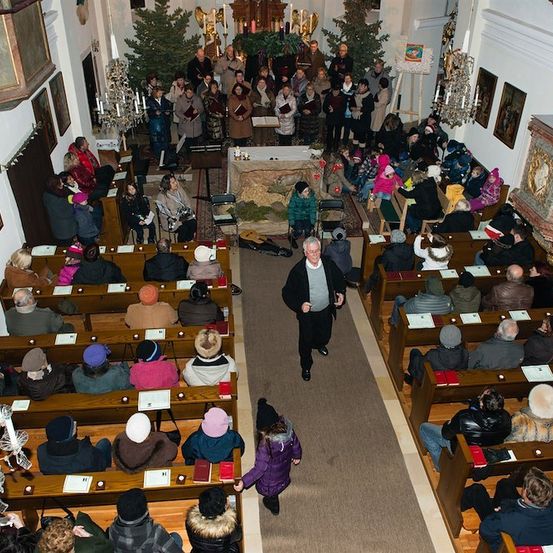 Eine Gemeinde in einer Kirche, mit einem Mann, der den Gang hinuntergeht. Viele Menschen sitzen auf Kirchenbänken, und einige stehen in der Nähe des Altars.