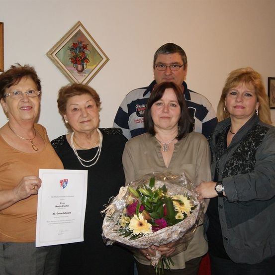 Fünf Erwachsene stehen zusammen, zwei Frauen halten ein Zertifikat und einen Blumenstrauß. Sie posieren für ein Foto.