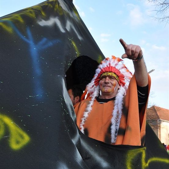Ein Mann in einem indianischen Federkopfschmuck zeigt auf etwas, während er in einem mit Graffiti bedeckten Zelt steht.