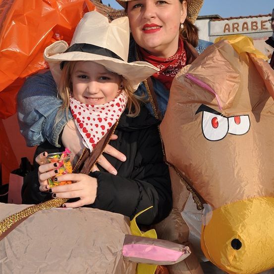 Eine Frau und ein junges Mädchen in Cowboy-Kostümen posieren neben aufblasbaren Tieren bei einer Veranstaltung im Freien.
