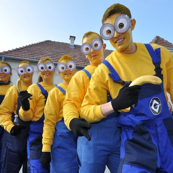 Eine Gruppe von Menschen, die als Minions aus dem Film Ich - Einfach unverbesserlich verkleidet sind, stehen vor einem Haus. Sie tragen alle gelbe Hemden, blaue Latzhosen und große runde Brillen. Einer von ihnen hält eine Banane.
