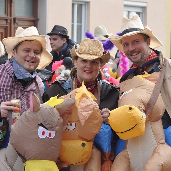 Drei Personen in Cowboyhüten und aufblasbaren Pferdekostümen posieren für ein Foto bei einer Veranstaltung im Freien.