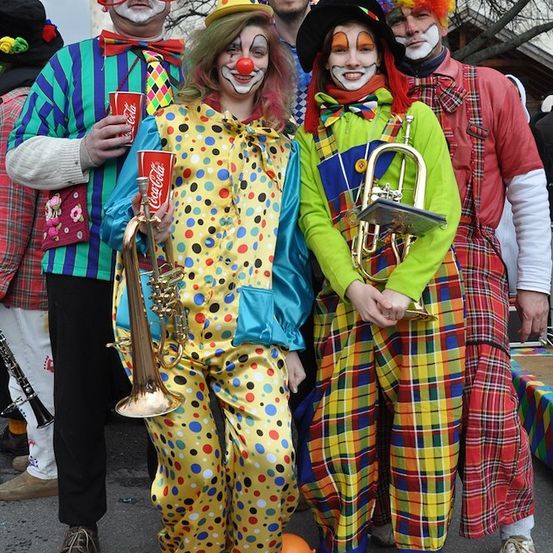 Eine Gruppe von Clowns in bunten Kostümen und mit geschminkten Gesichtern, die Musikinstrumente und Coca-Cola-Becher halten und für ein Foto posieren.