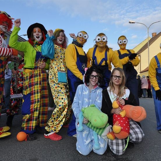 Eine Gruppe von Menschen in verschiedenen Kostümen, darunter Clowns, Minions und ein Mädchen im Pyjama, posiert für ein Foto im Freien.