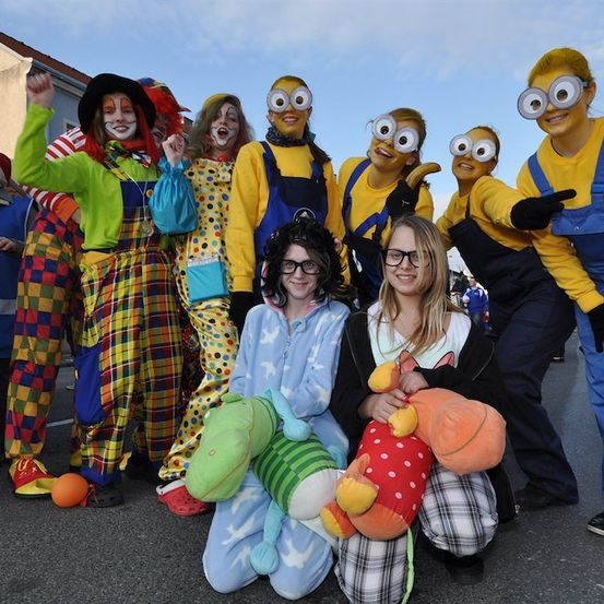 Eine Gruppe von Menschen in Kostümen, darunter Clowns und Minions, posiert für ein Foto. Zwei Mädchen vorne halten Plüschtiere.