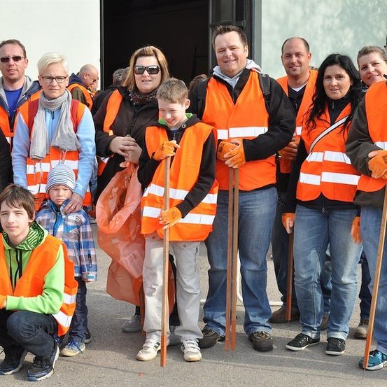 Eine Gruppe von Menschen in orangefarbenen Westen und mit Stöcken posiert für ein Foto. Einige knien, und ein Junge trägt einen Hut. Sie sind wahrscheinlich Freiwillige für einen Gemeinschaftsdienst.