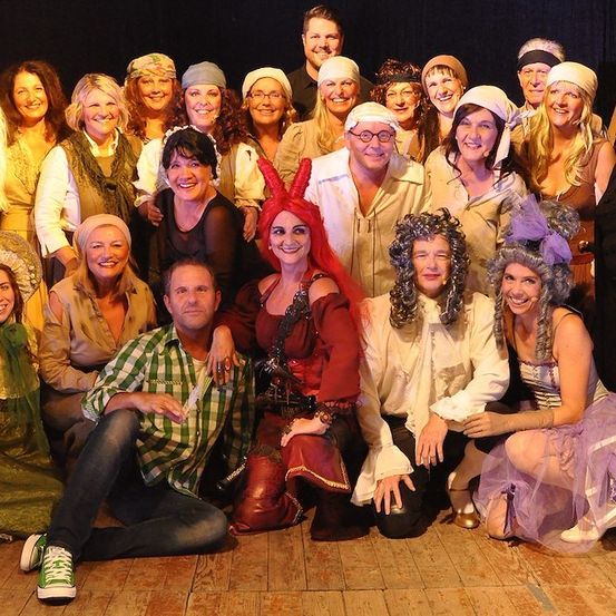 Eine Gruppe von Menschen in Kostümen, wahrscheinlich für ein Theaterstück, posiert für ein Foto auf einem Holzboden.