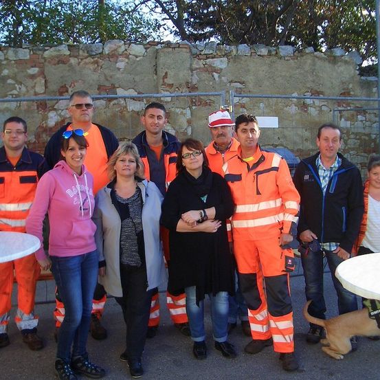 Eine Gruppe von Menschen, darunter sowohl Männer als auch Frauen, stehen zusammen vor einer Steinmauer. Sie tragen Sicherheitswesten und scheinen für ein Foto zu posieren.