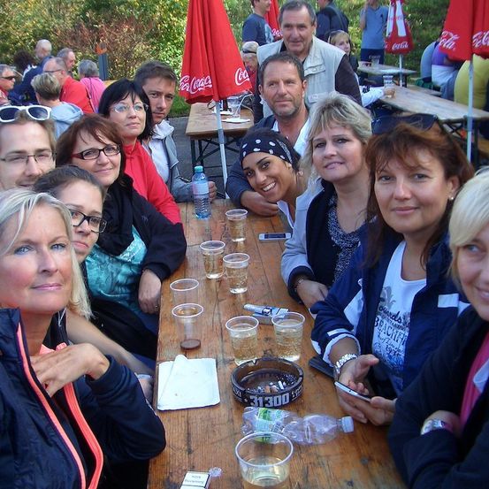 Eine Gruppe von Menschen sitzt um einen Tisch mit Getränken und einer Aschenschale und posiert für ein Foto.