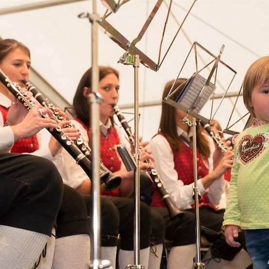 Eine Gruppe junger Frauen in traditioneller Kleidung spielt Klarinetten in einer Band, mit einem kleinen Mädchen vorne, das sie beobachtet.