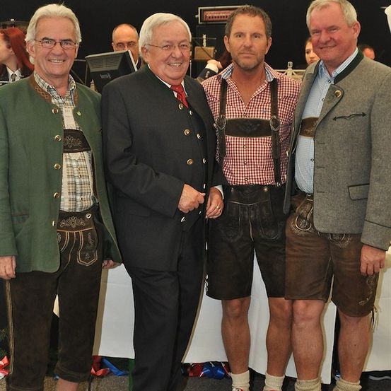 Vier Männer in traditioneller deutscher Kleidung, möglicherweise bei einem Fest, stehen zusammen und lächeln für ein Foto.