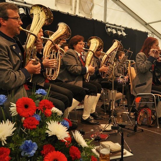Eine Gruppe von Musikern spielt Blechblasinstrumente auf einer Bühne mit einem Blumenstrauß im Vordergrund.
