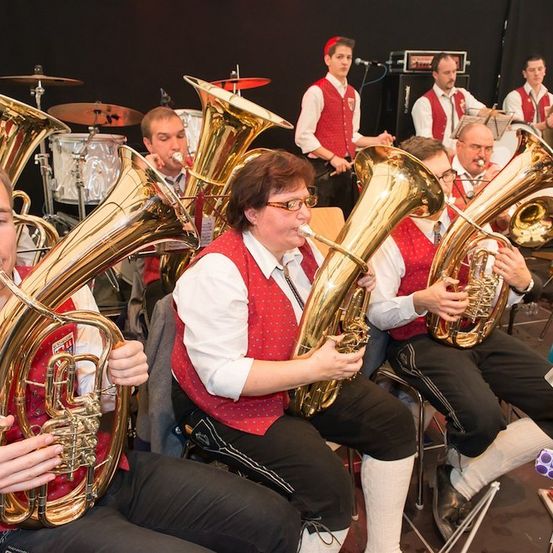 Ein Brass-Band spielt auf der Bühne, mit Musikern, die Tubas und andere Instrumente spielen. Die Bandmitglieder sind in traditioneller Kleidung gekleidet.