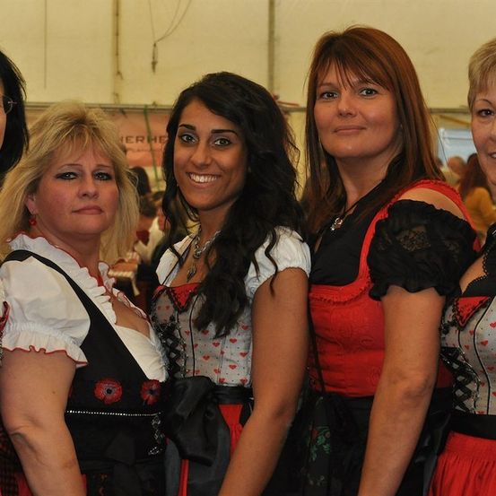 Fünf Frauen in traditioneller deutscher Kleidung, lächelnd und posierend für ein Foto bei einer Veranstaltung.